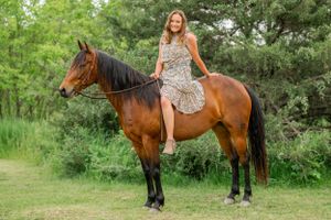 A rider in a floral dress sits bareback on a bay horse against a green summer backdrop.
