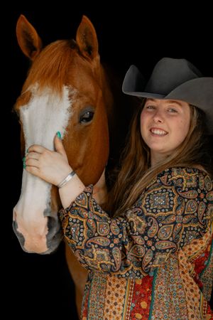 A chestnut horse with white blaze poses with someone in a patterned shirt and cowboy hat.