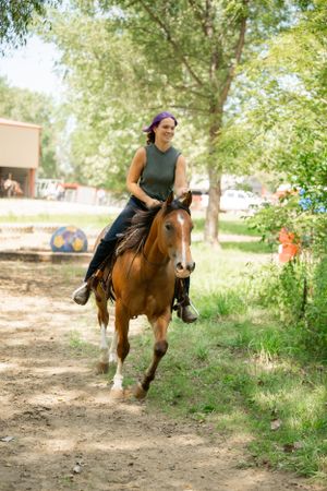 A rider in a gray tank top gallops along a dirt trail on a chestnut horse.