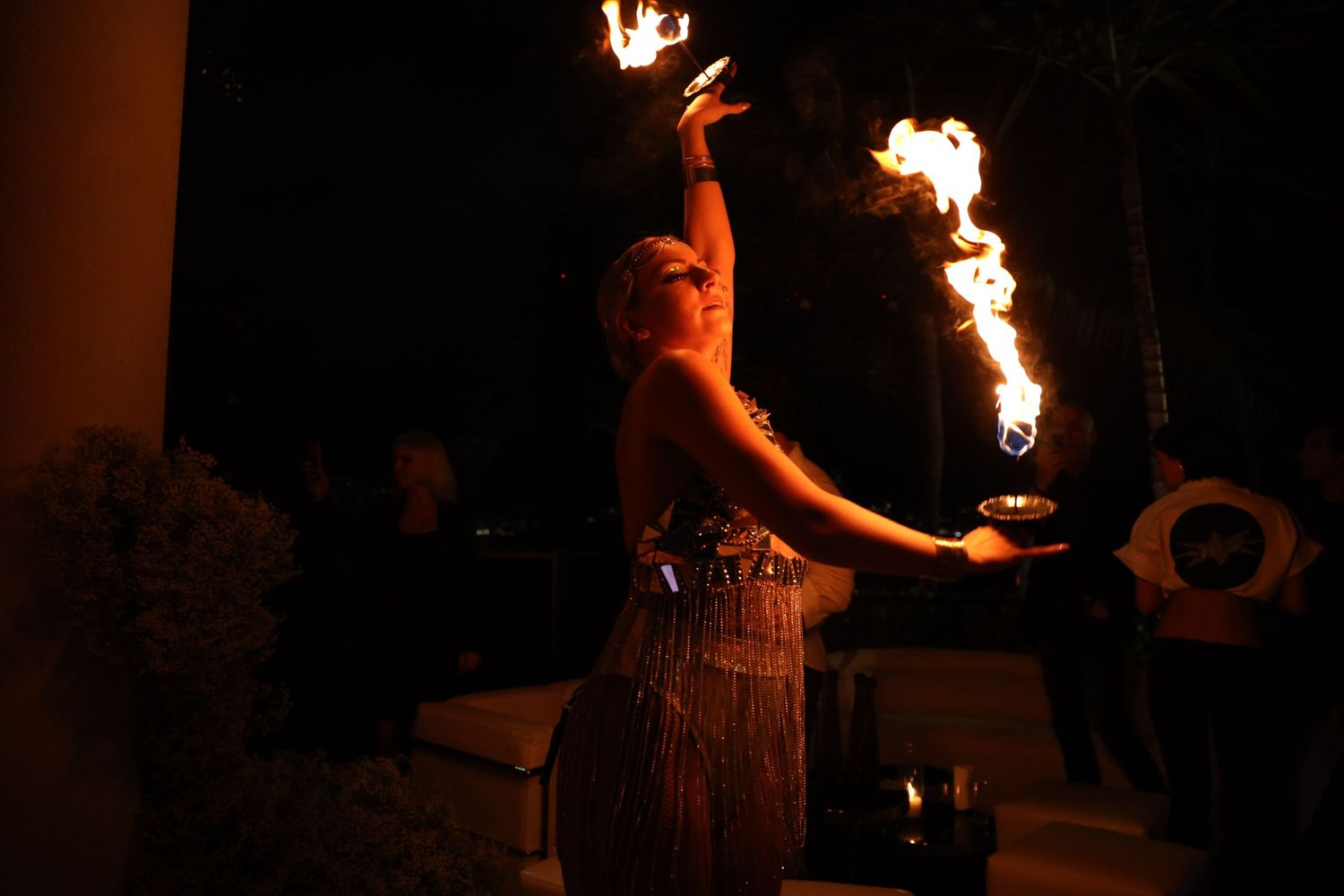 Fire dancer performs with flaming torches at night while wearing a grass skirt during an entertainment show.