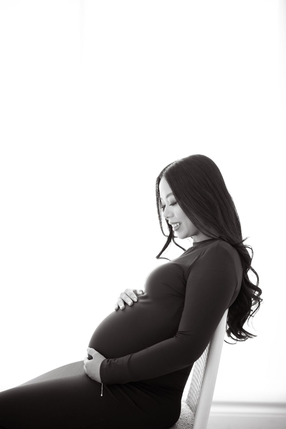 Black and white maternity photo of an expectant mother in a dark sweater sitting in profile.