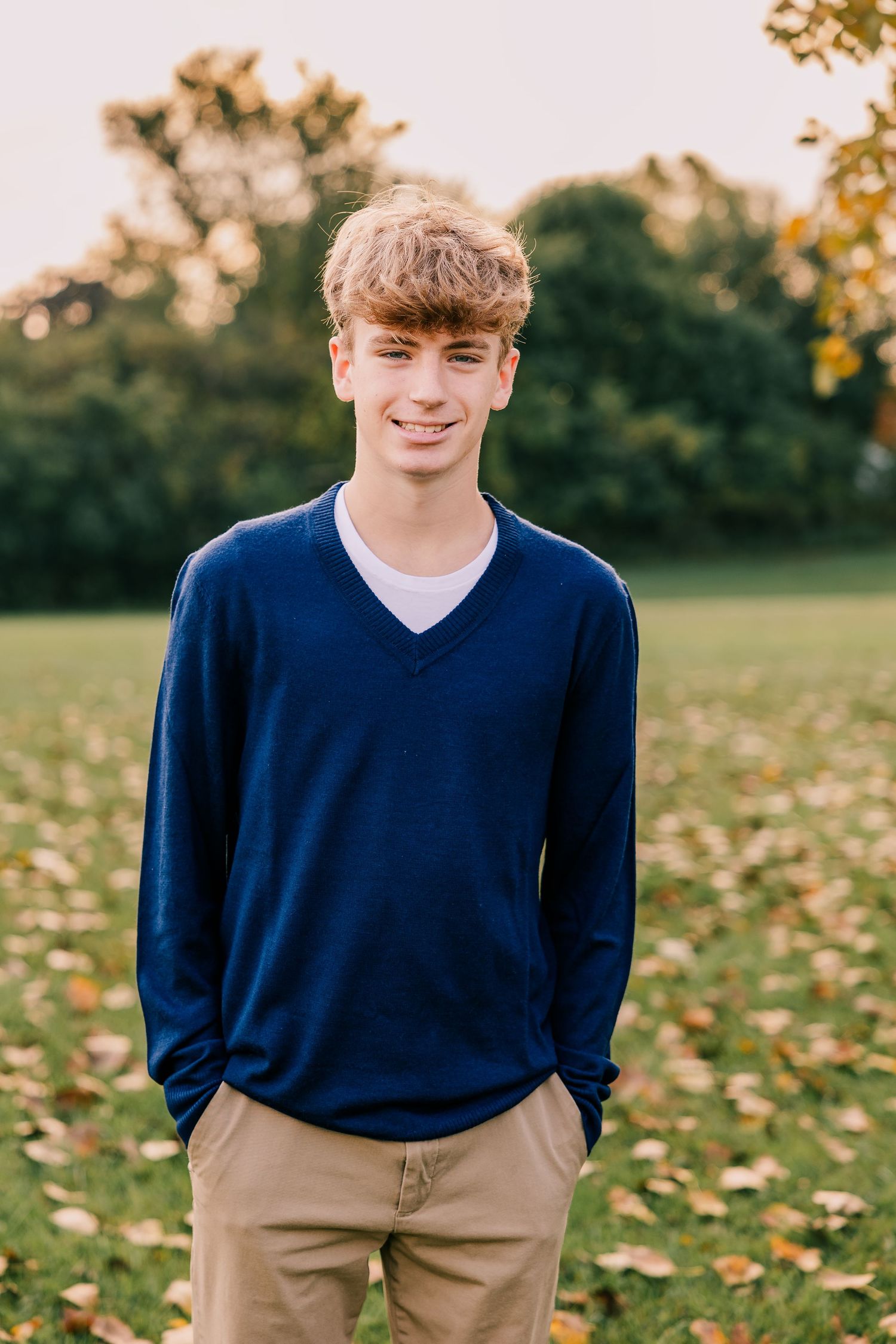 Teen boy in navy v-neck sweater poses outdoors during autumn. Portraits by Rachel Martinez Photography.