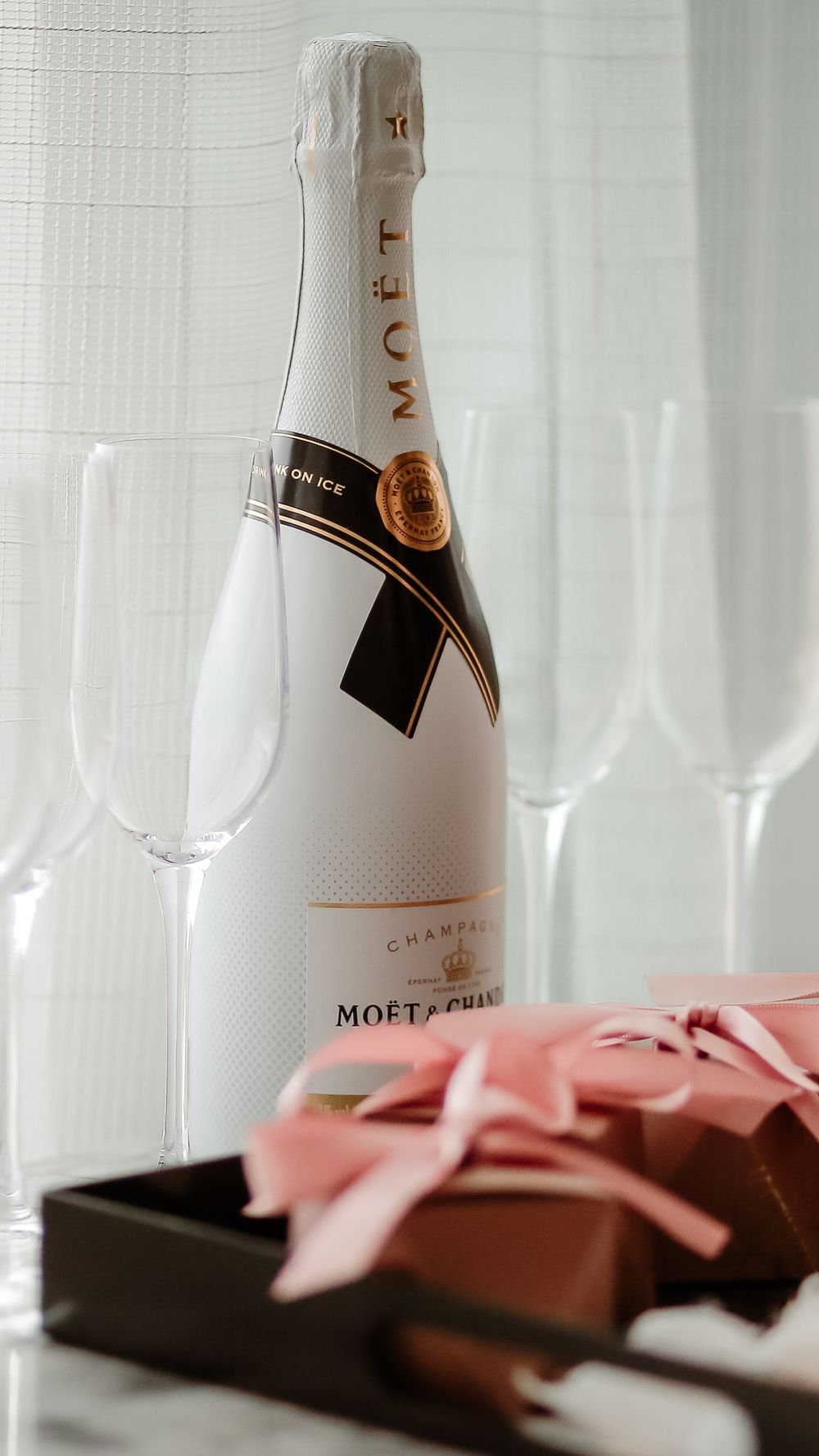 Moet & Chandon champagne bottle with empty flutes and a gift box with pink bow.