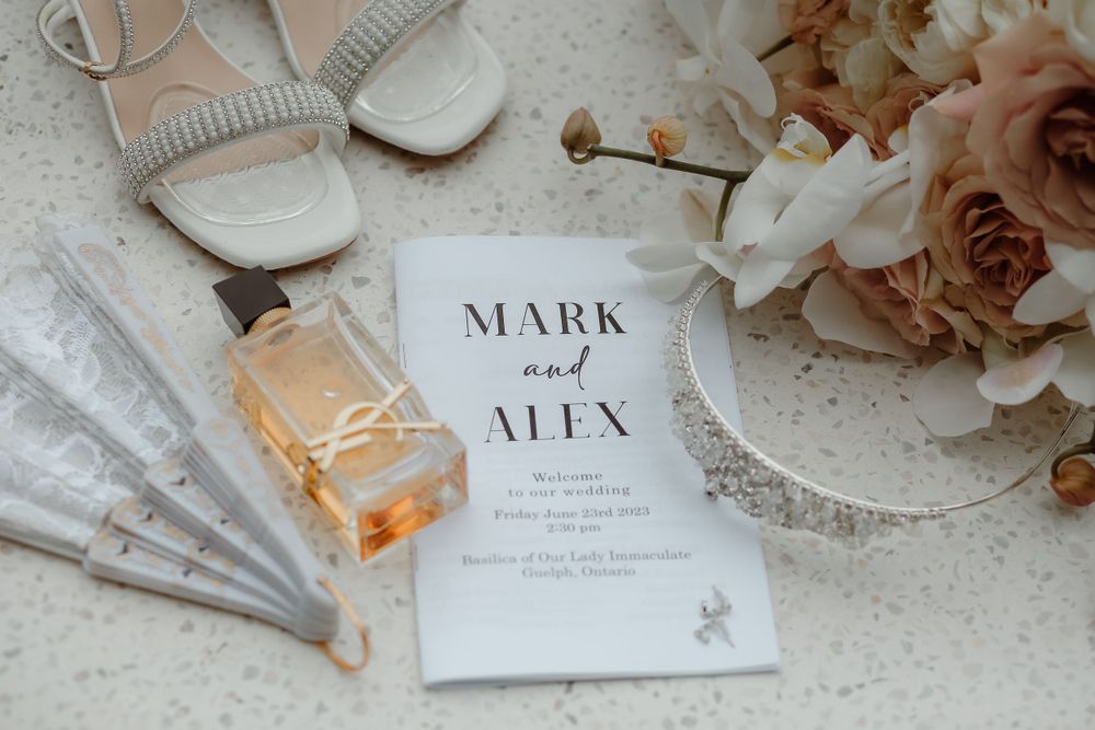Wedding details flatlay with invitation, perfume, shoes and blush roses.