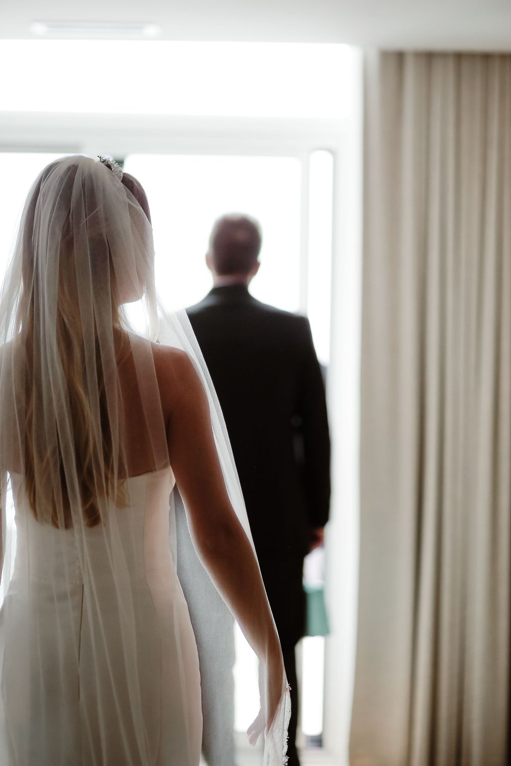 Silhouette of bride in wedding gown and groom standing by window.