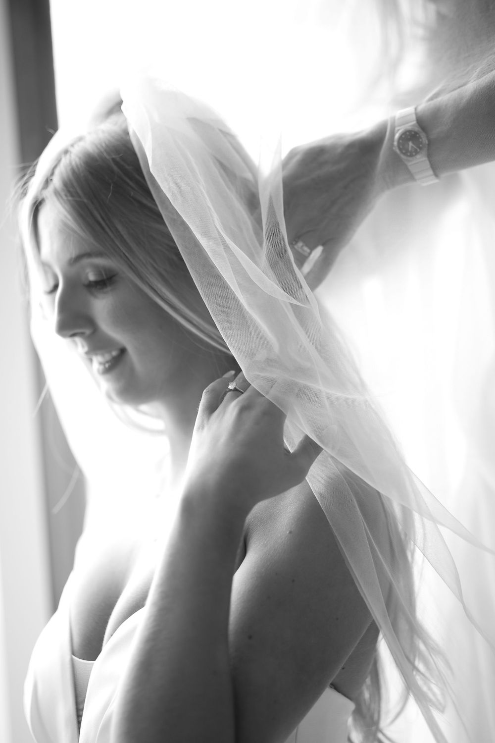 Artistic black and white portrait of bride with flowing veil in natural window light.