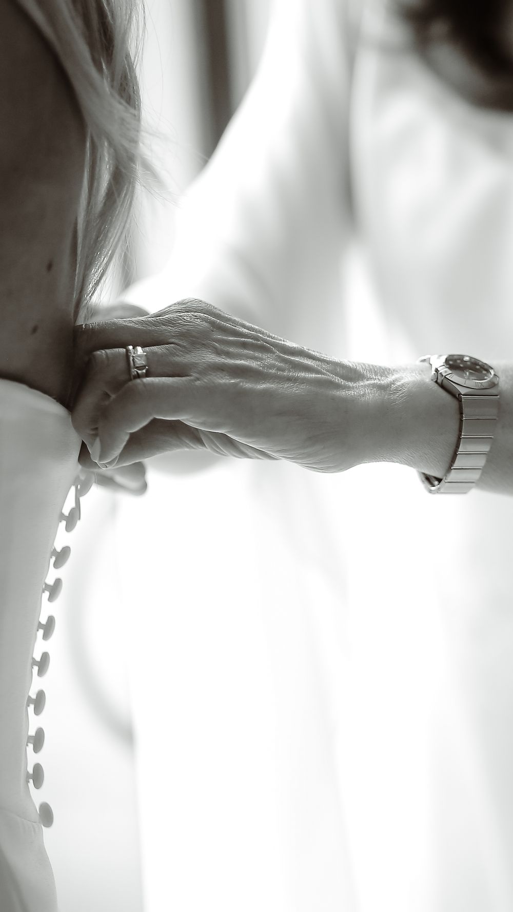 Close-up of hands buttoning white wedding dress with pearl details.