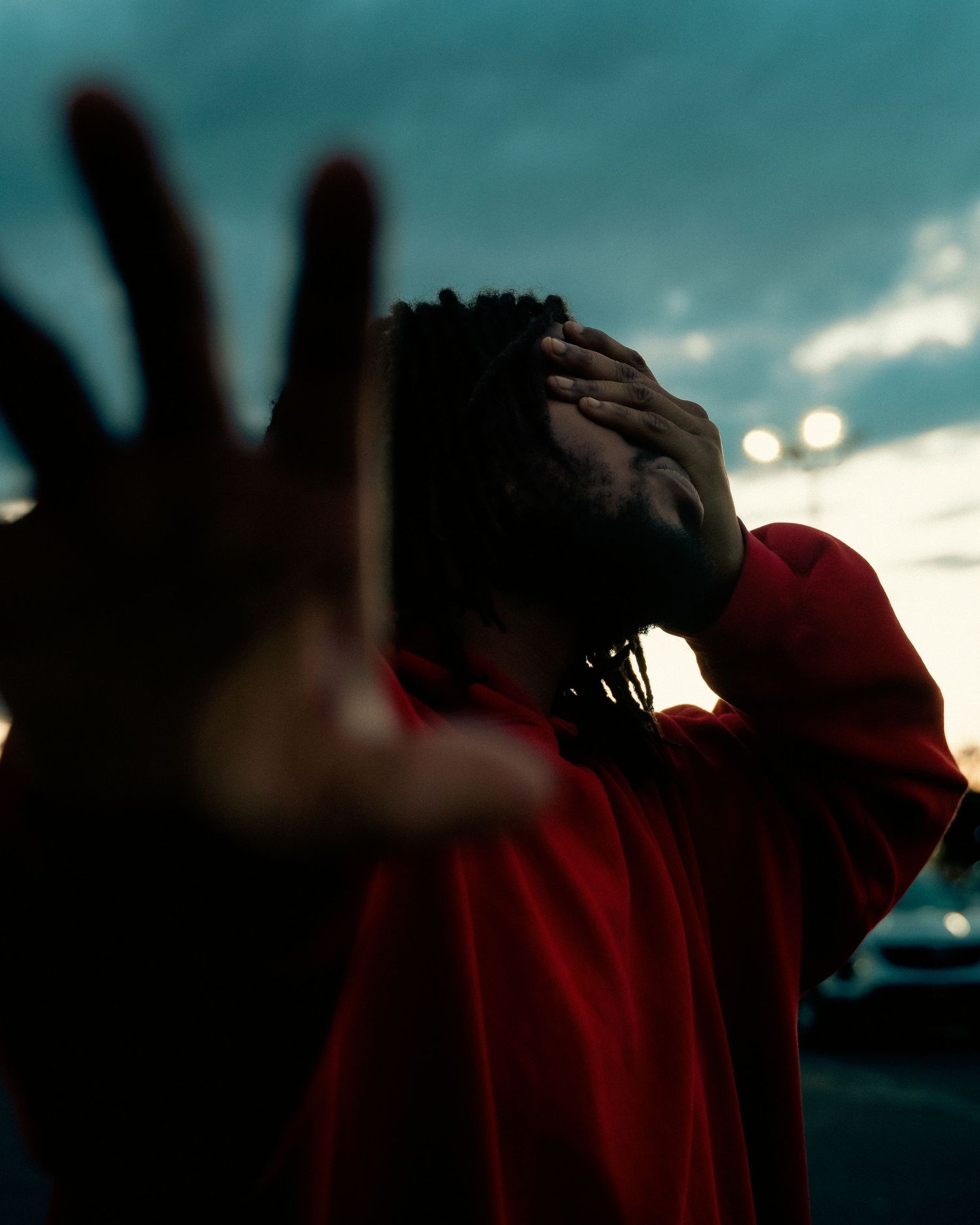Silhouetted figure in red hoodie reaching out against dramatic sunset sky.
