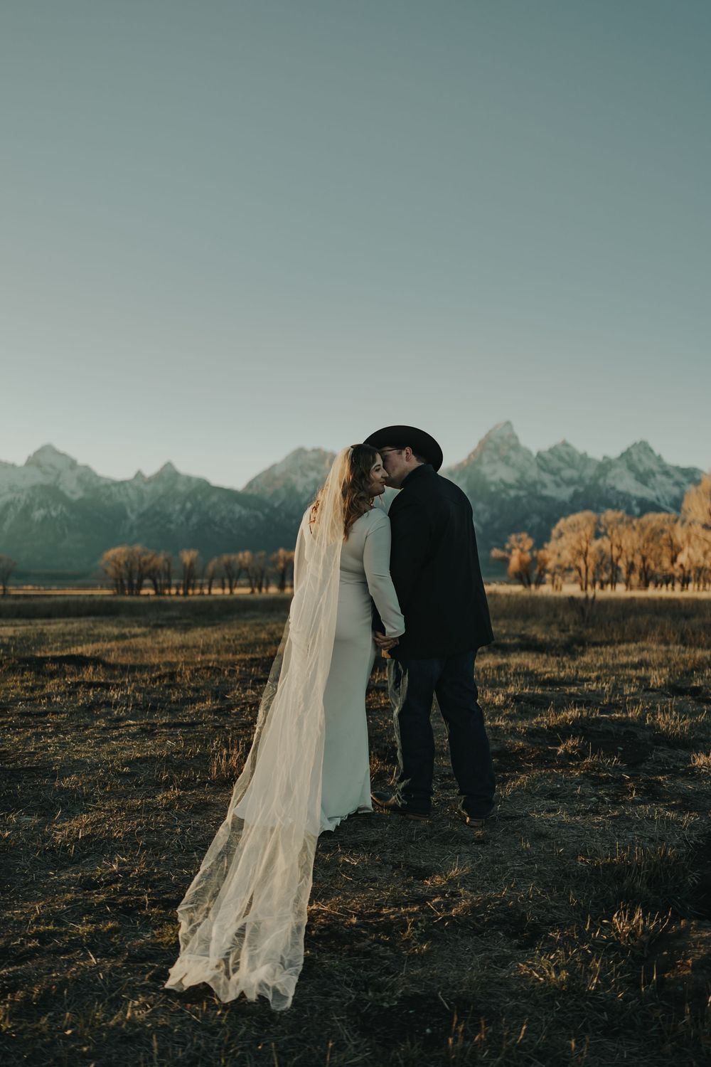 Bride and groom kissing in a field with the Grand Teton mountains in the background during golden hour.
