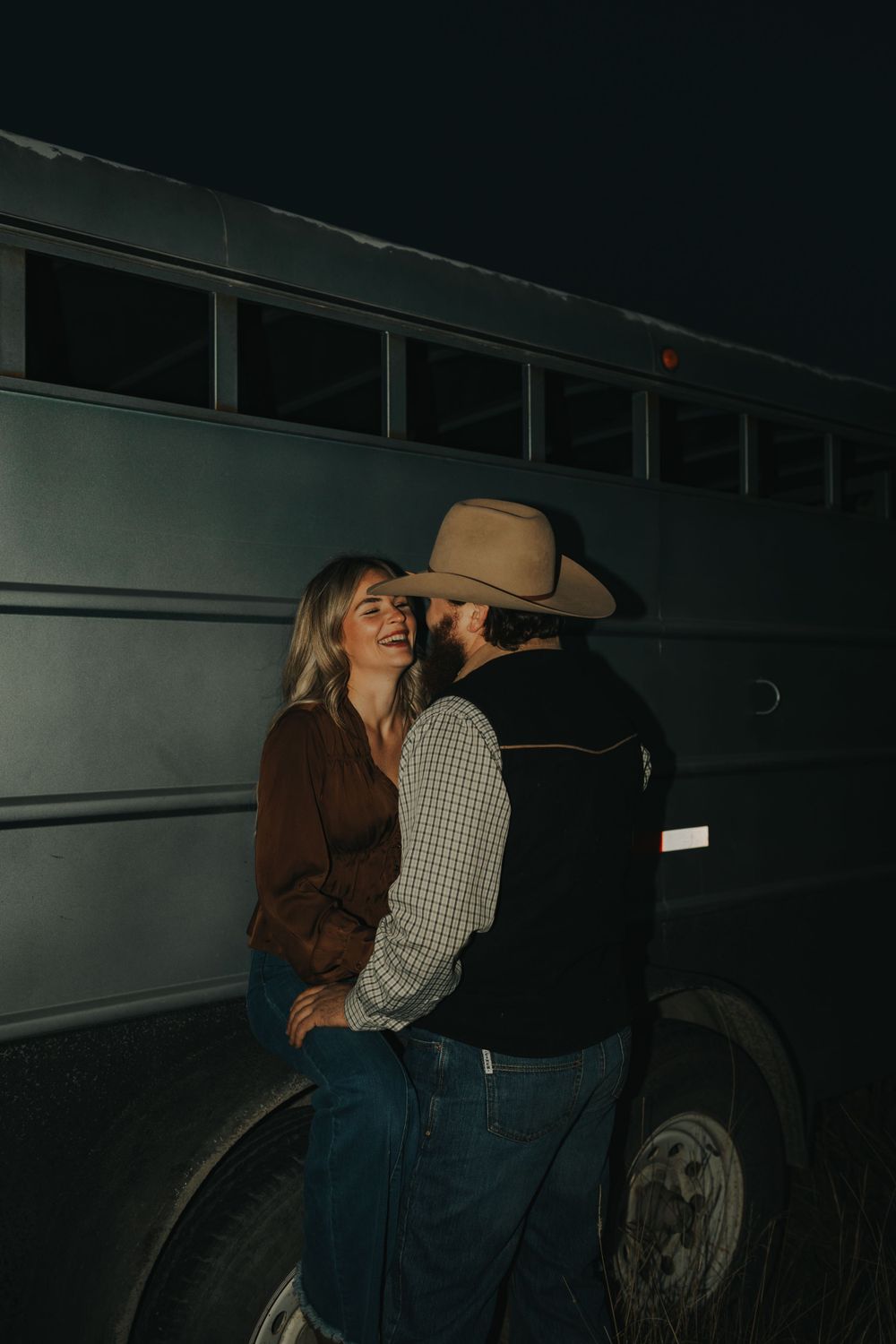 A couple shares an intimate moment next to a vintage bus at night.
