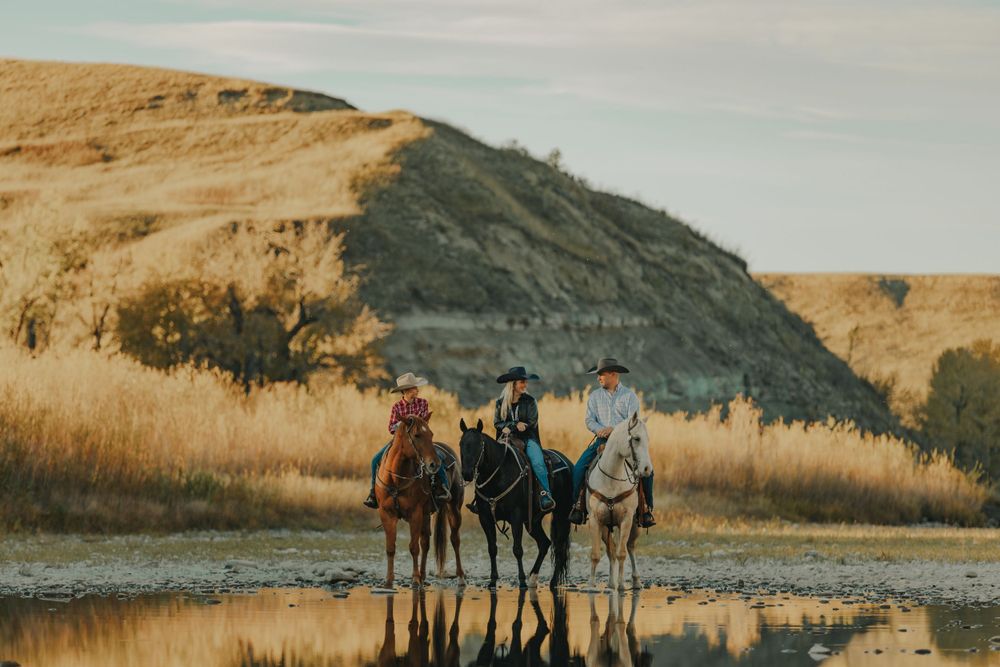 family photoshoot along the riverbank as they stand in reflective water against a golden hillside at sunset.