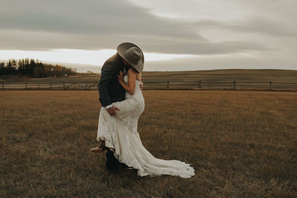 A couple embraces in formal attire on a ranch with moody skies overhead.