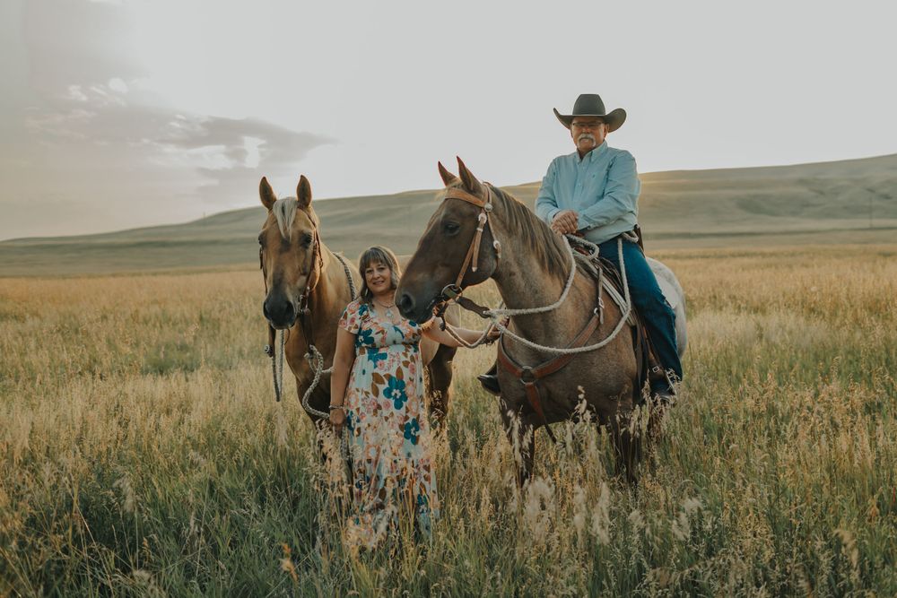 Two people on horseback pause in a sunlit prairie field.