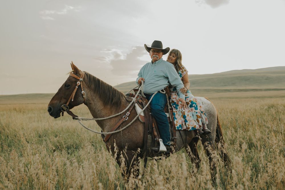 Two riders on horseback traverse through a scenic grassland prairie at sunset.