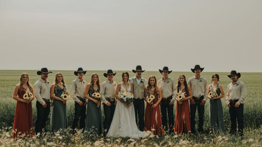 Wedding party in cowboy hats poses together in an open field.