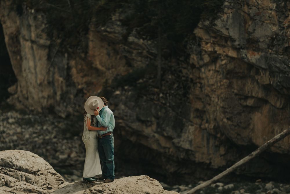 Couple embracing on rocky cliff edge with dramatic mountain backdrop.