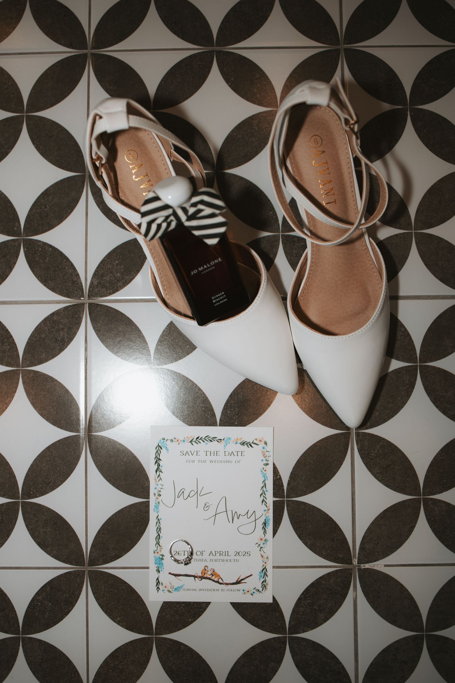 White bridal shoes and wedding invitation cards arranged on geometric patterned floor tiles.
