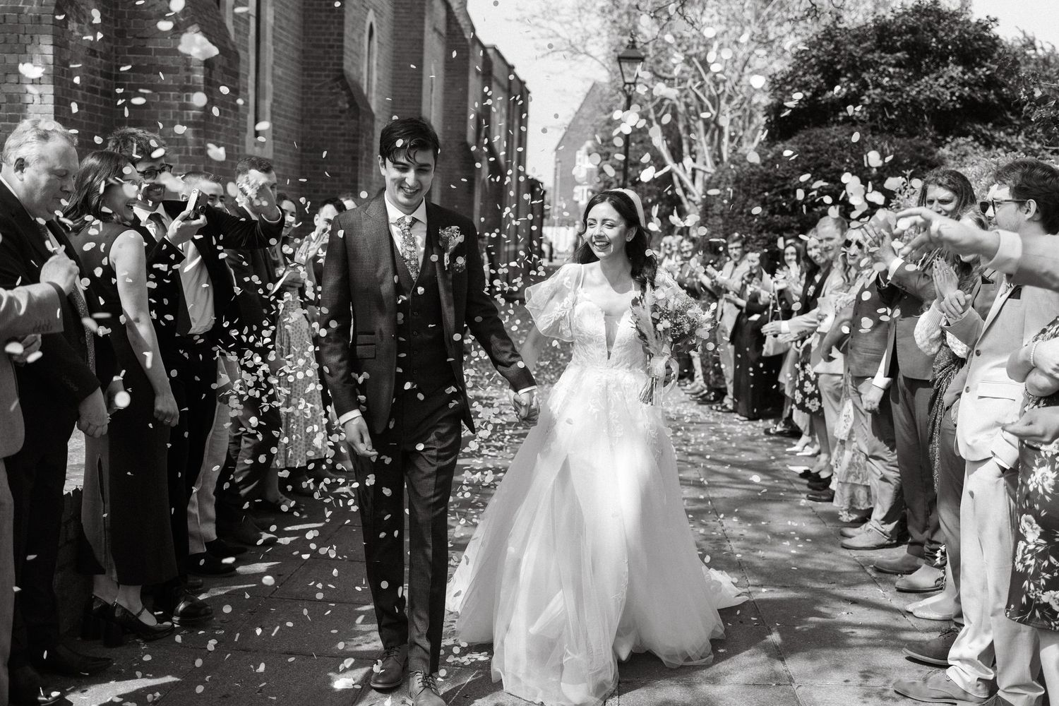 Black and white sequence of newlyweds walking through confetti shower with guests cheering.