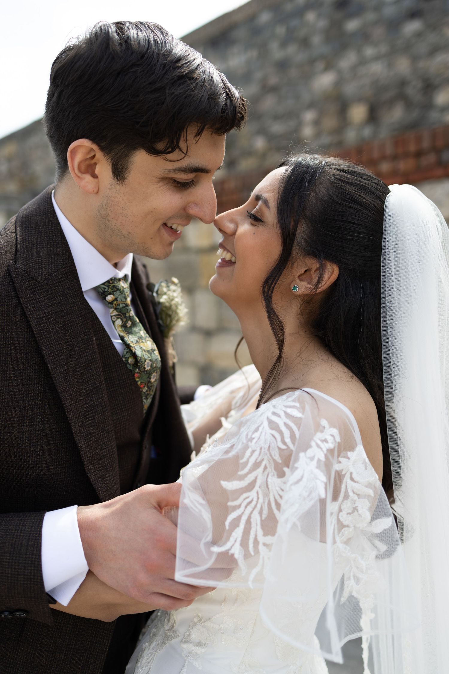 A romantic wedding portrait of a couple sharing an intimate moment against a stone wall background.