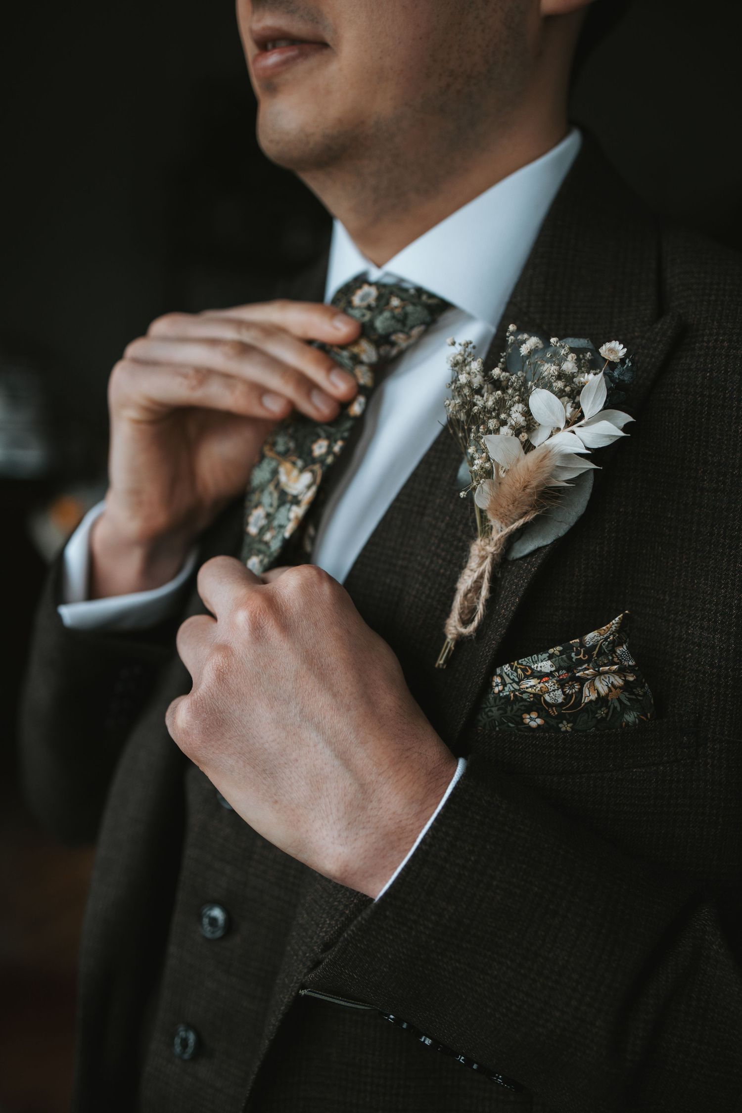 Close-up shots of a boutonniere and tie adjustment on a dark suit.