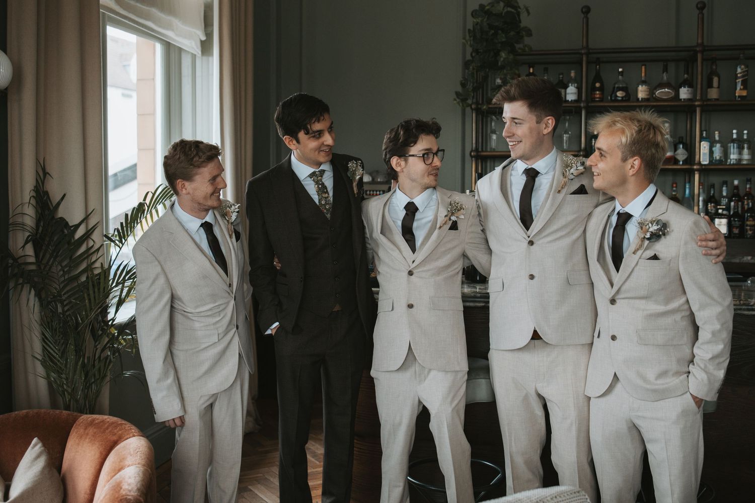 Wedding party in light gray suits posing together in an indoor venue.