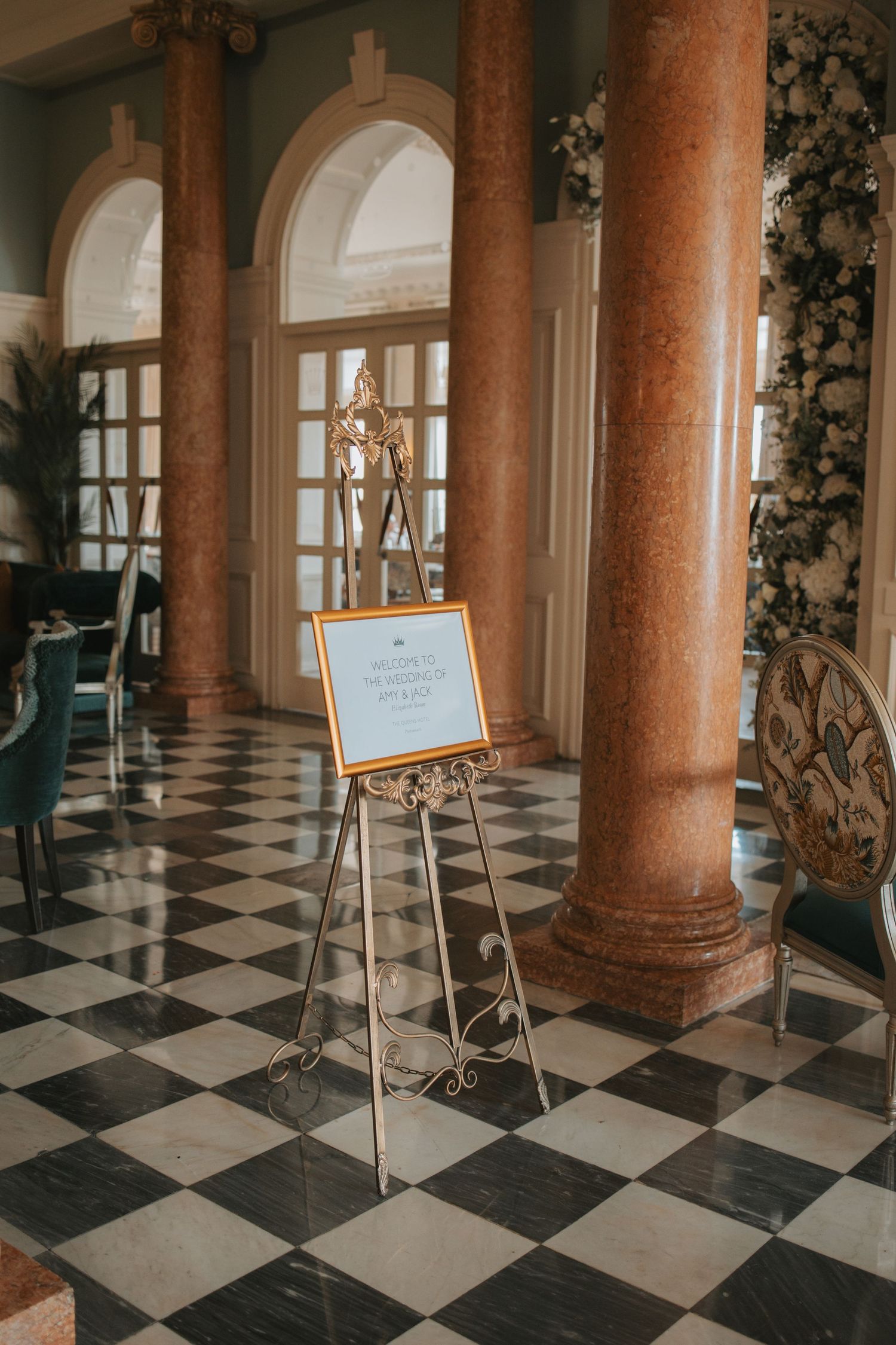 Grand ballroom with ornate columns and black and white checkered flooring.