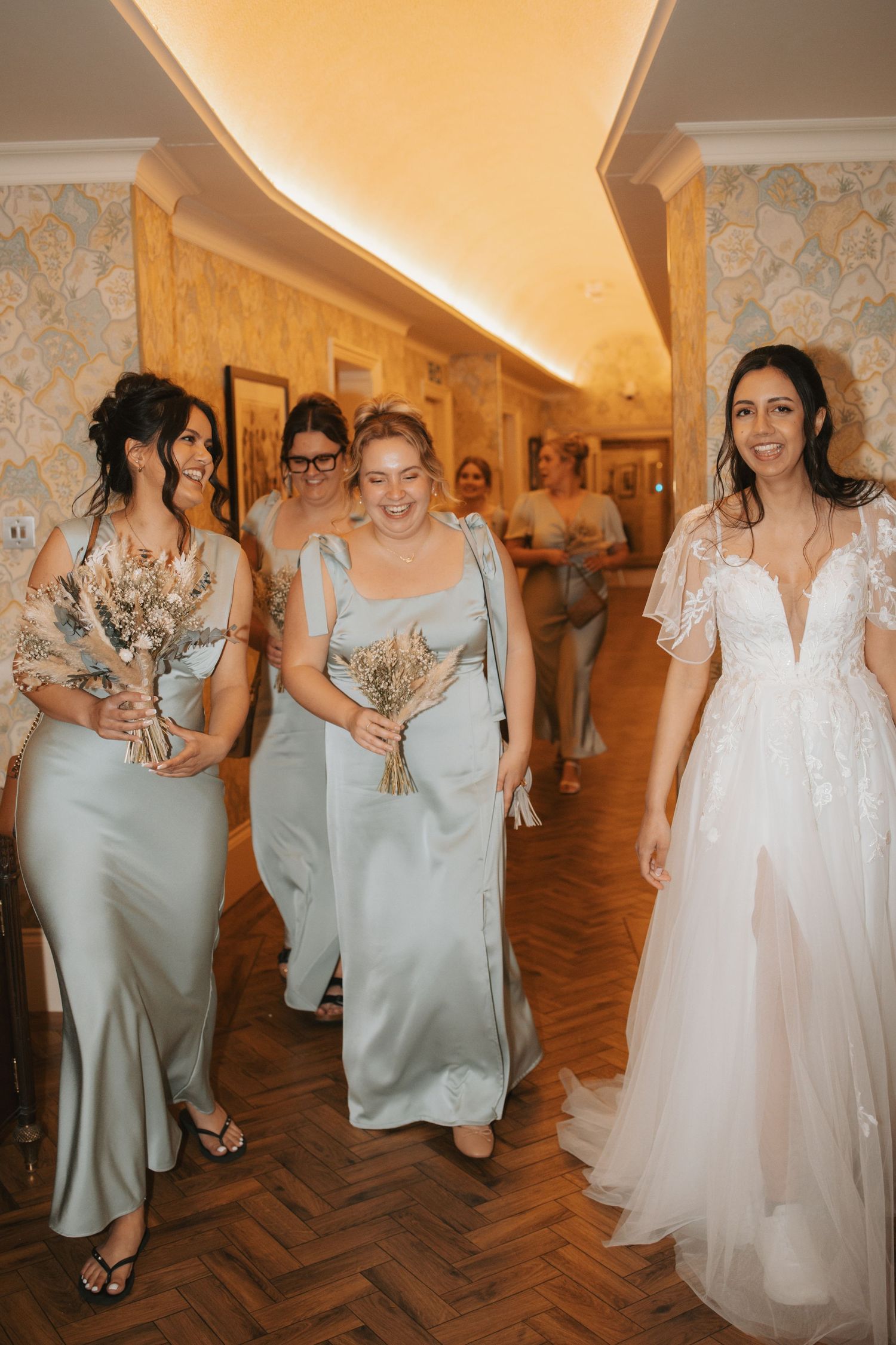 Bridesmaids in sage green dresses walking with the bride in a wedding gown.