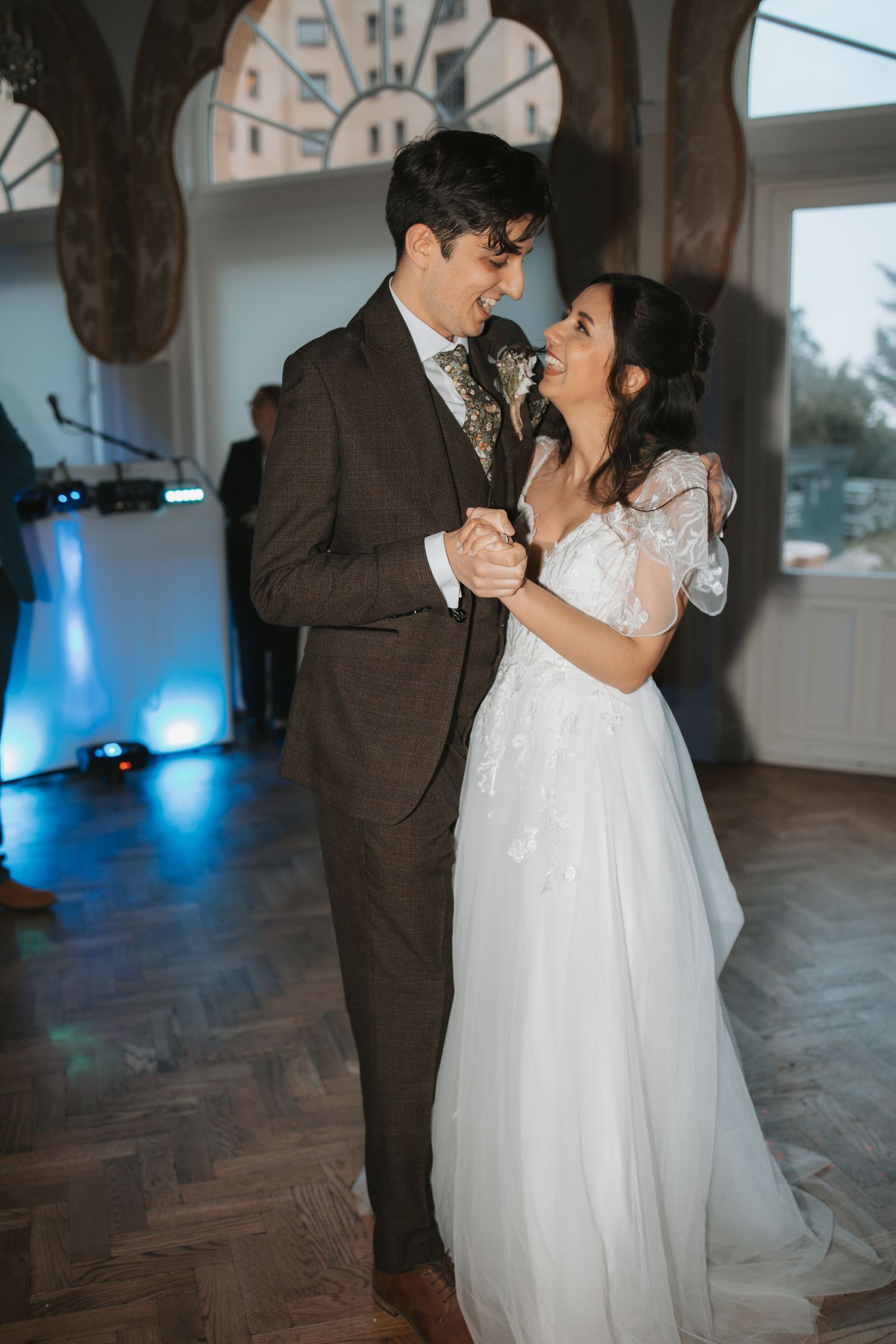 Wedding couple sharing a romantic dance moment in an elegant ballroom with natural lighting.