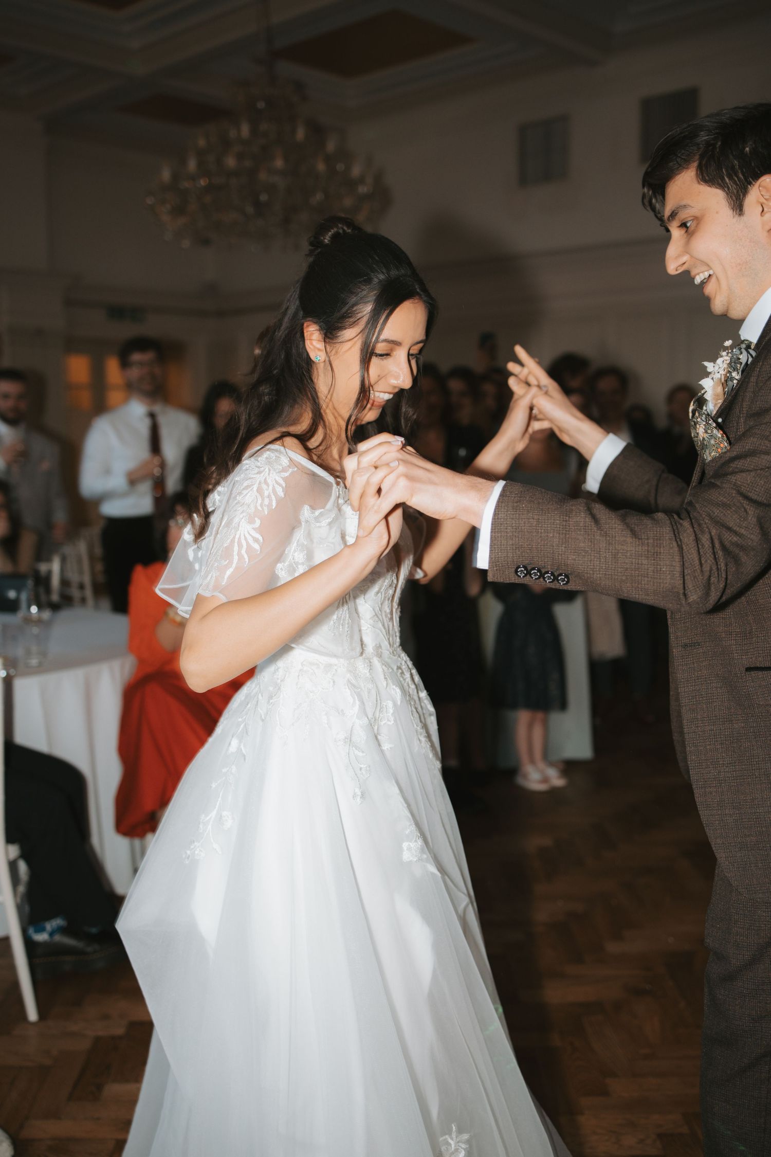 A couple dancing together at their wedding reception under an elegant chandelier.