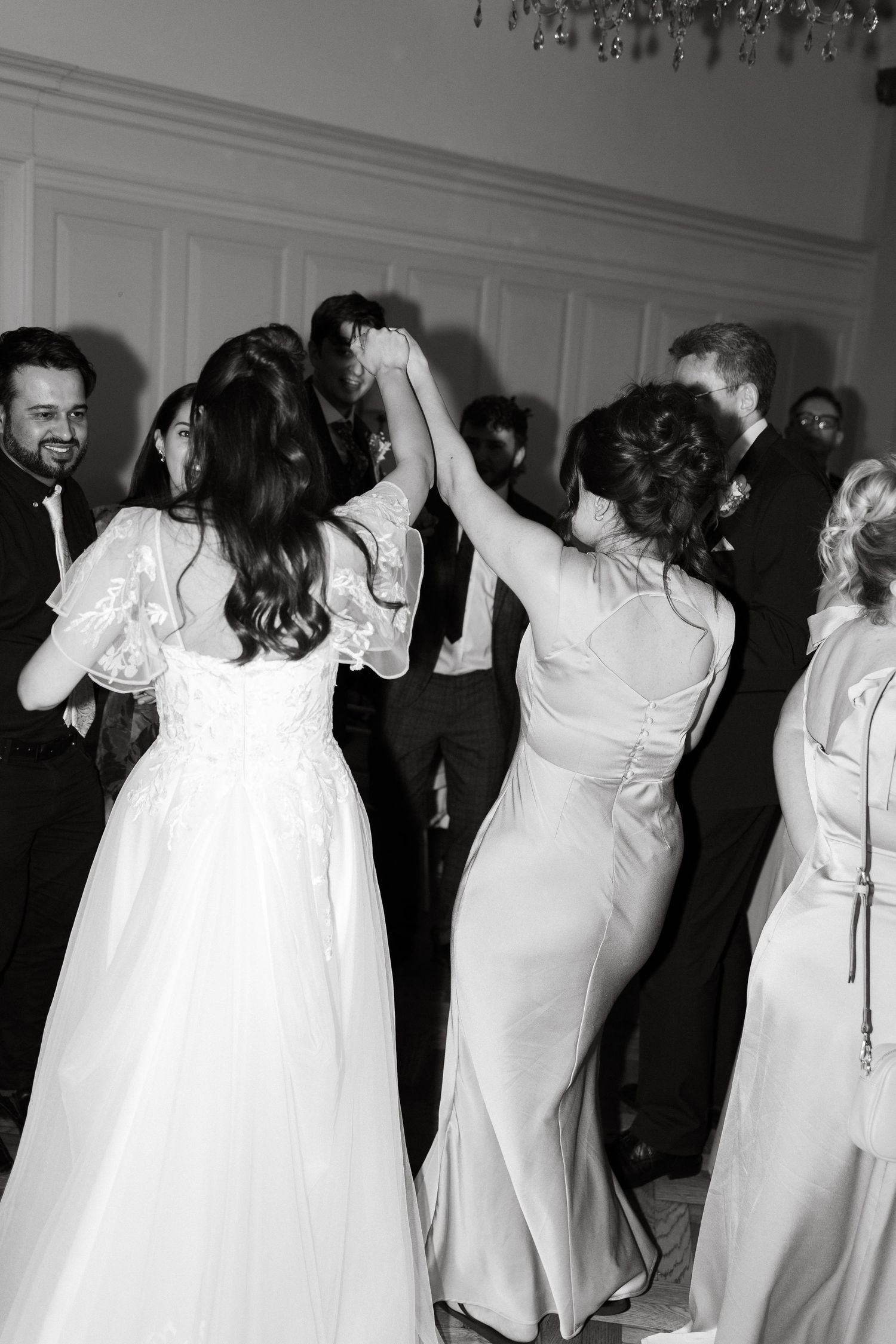 Wedding party members in white dresses dancing together at a reception celebration.