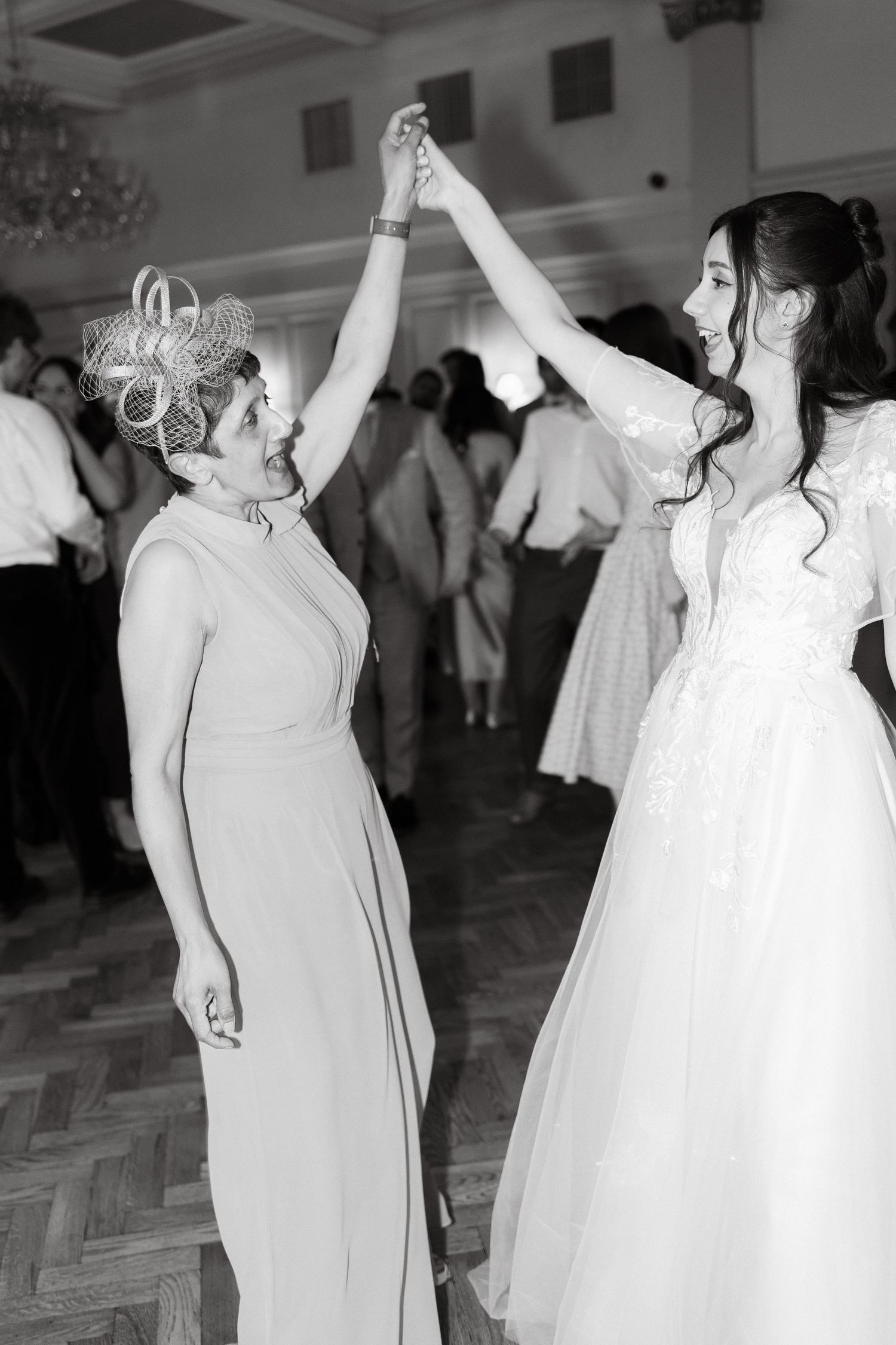 Women in light-colored dresses dancing with raised arms at a wedding celebration.