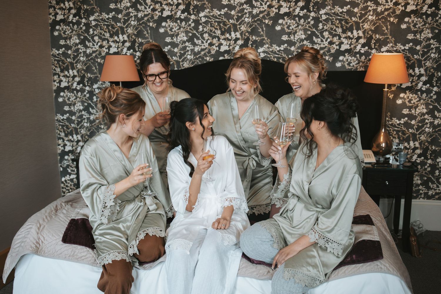 Bridesmaids in matching robes sharing joyful moments on a bed.