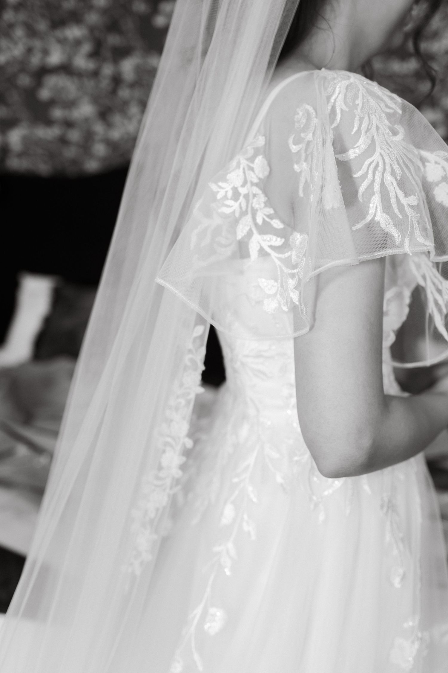 Intricate floral lace details adorn the sleeves and bodice of a flowing white wedding gown.