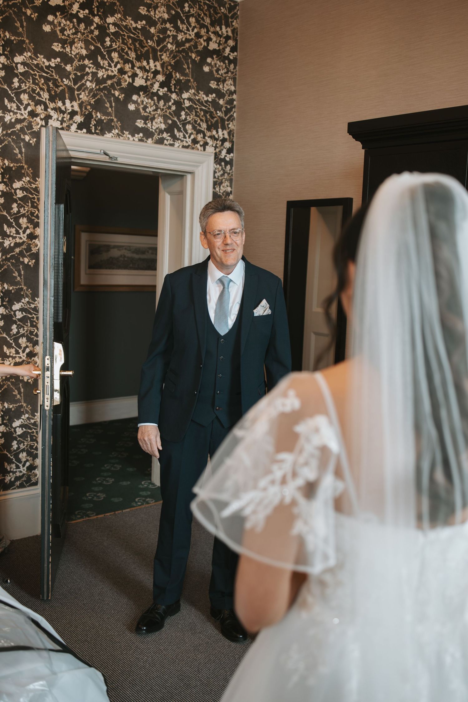 Emotional first look sequence in a room with floral wallpaper.