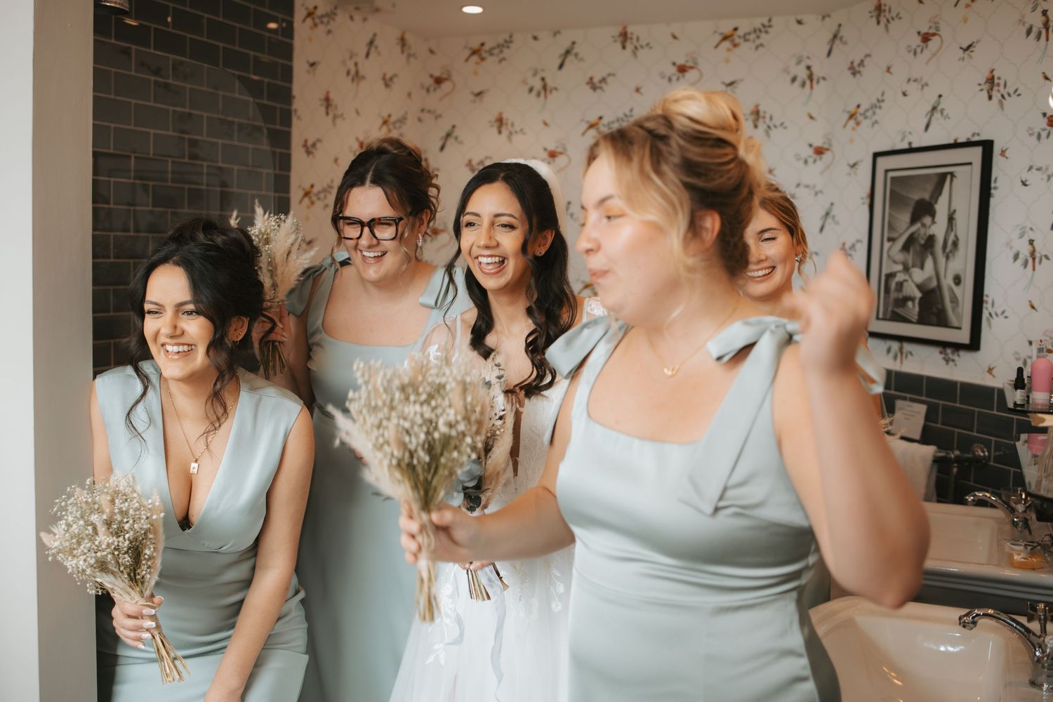 Bridesmaids in sage green dresses sharing joyful moments during wedding preparations.