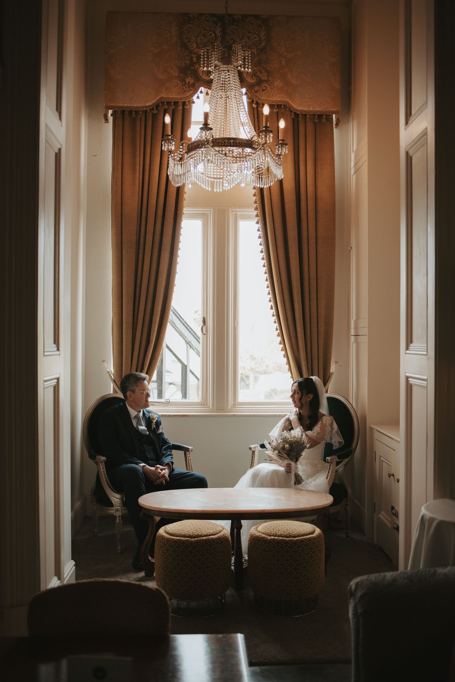 An elegant room with crystal chandeliers and floor-length curtains sets a romantic wedding day scene.