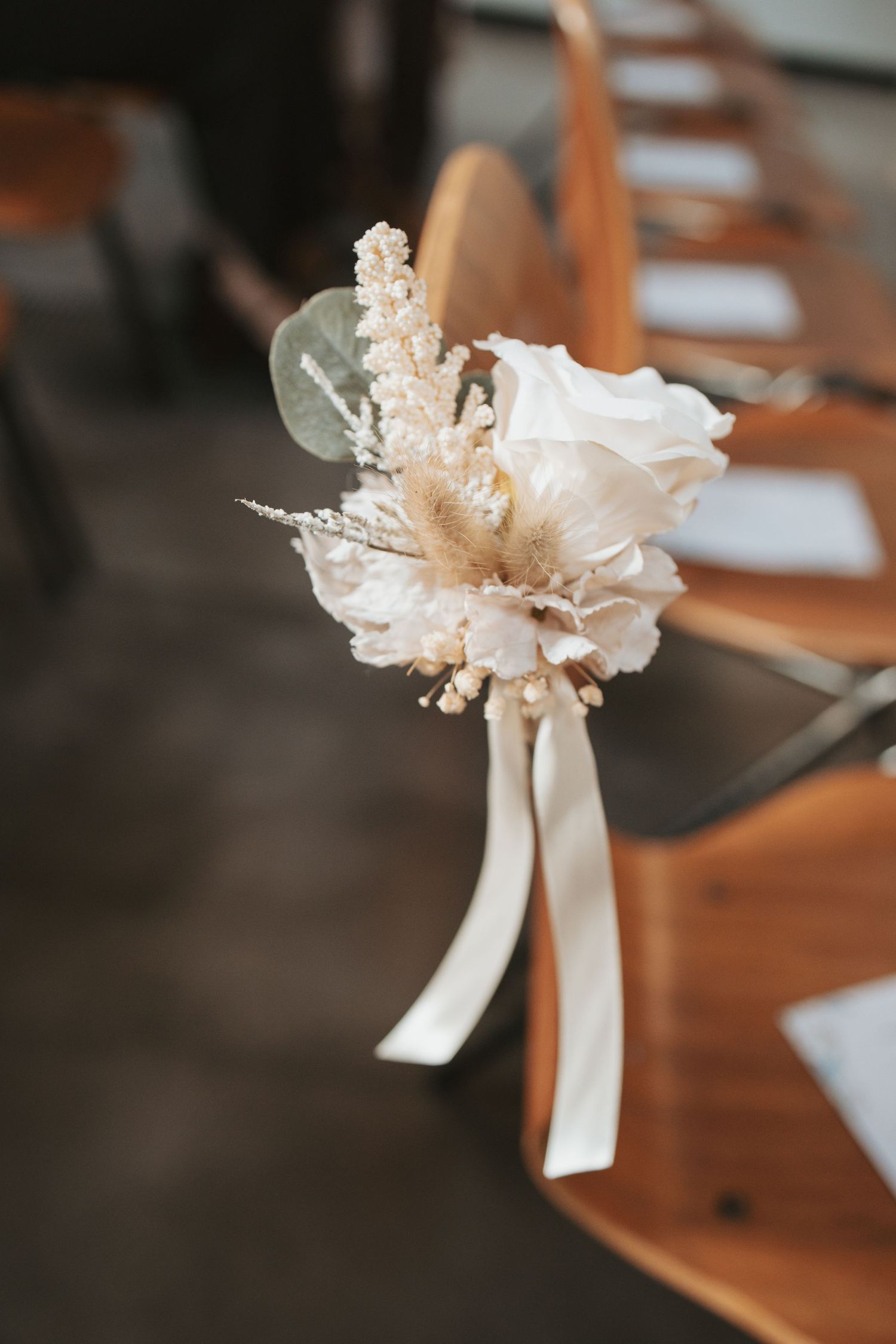 Delicate white floral pew decorations with ribbons adorn church seats.