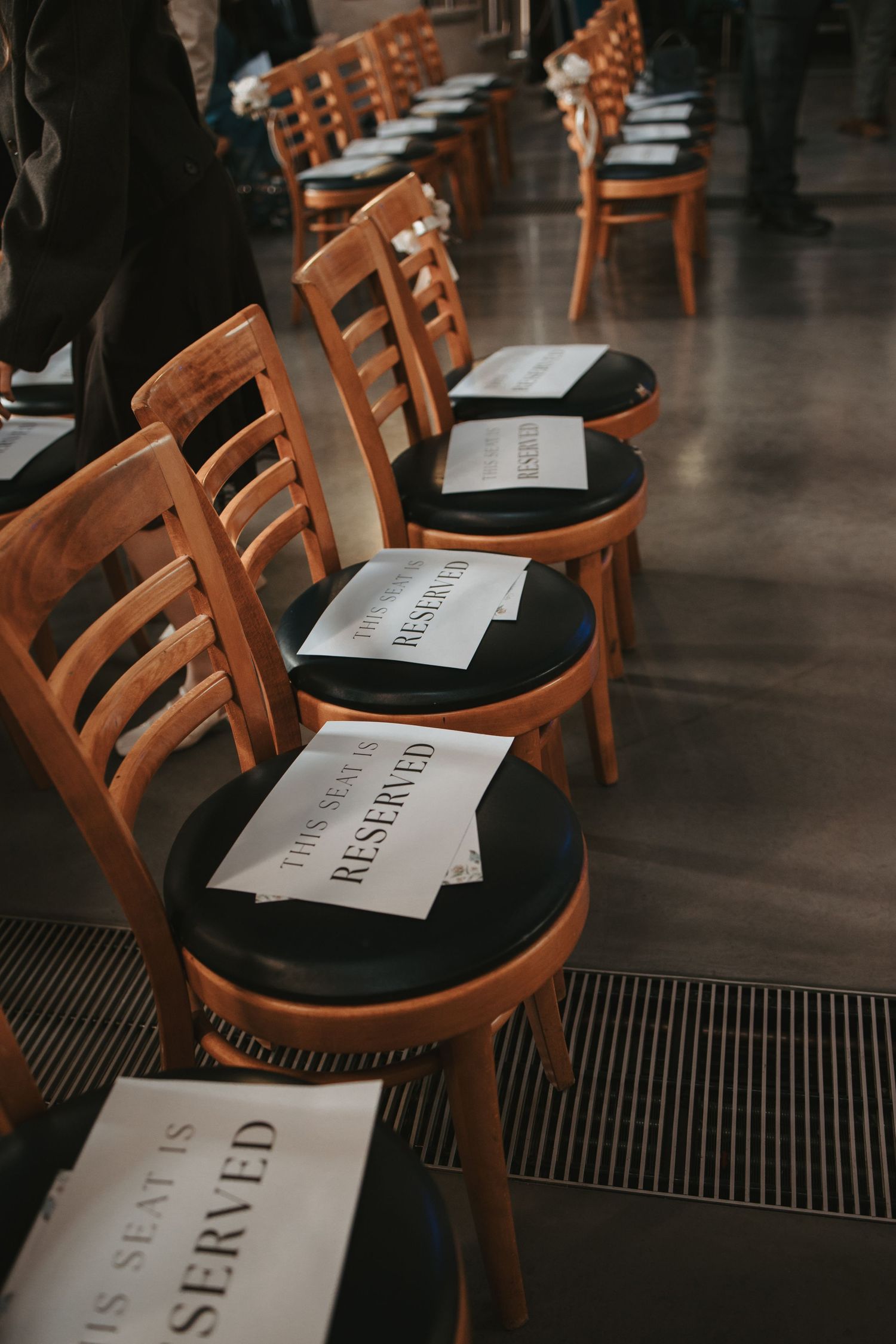 Wooden chairs with reserved signs line up in neat rows for a wedding ceremony.