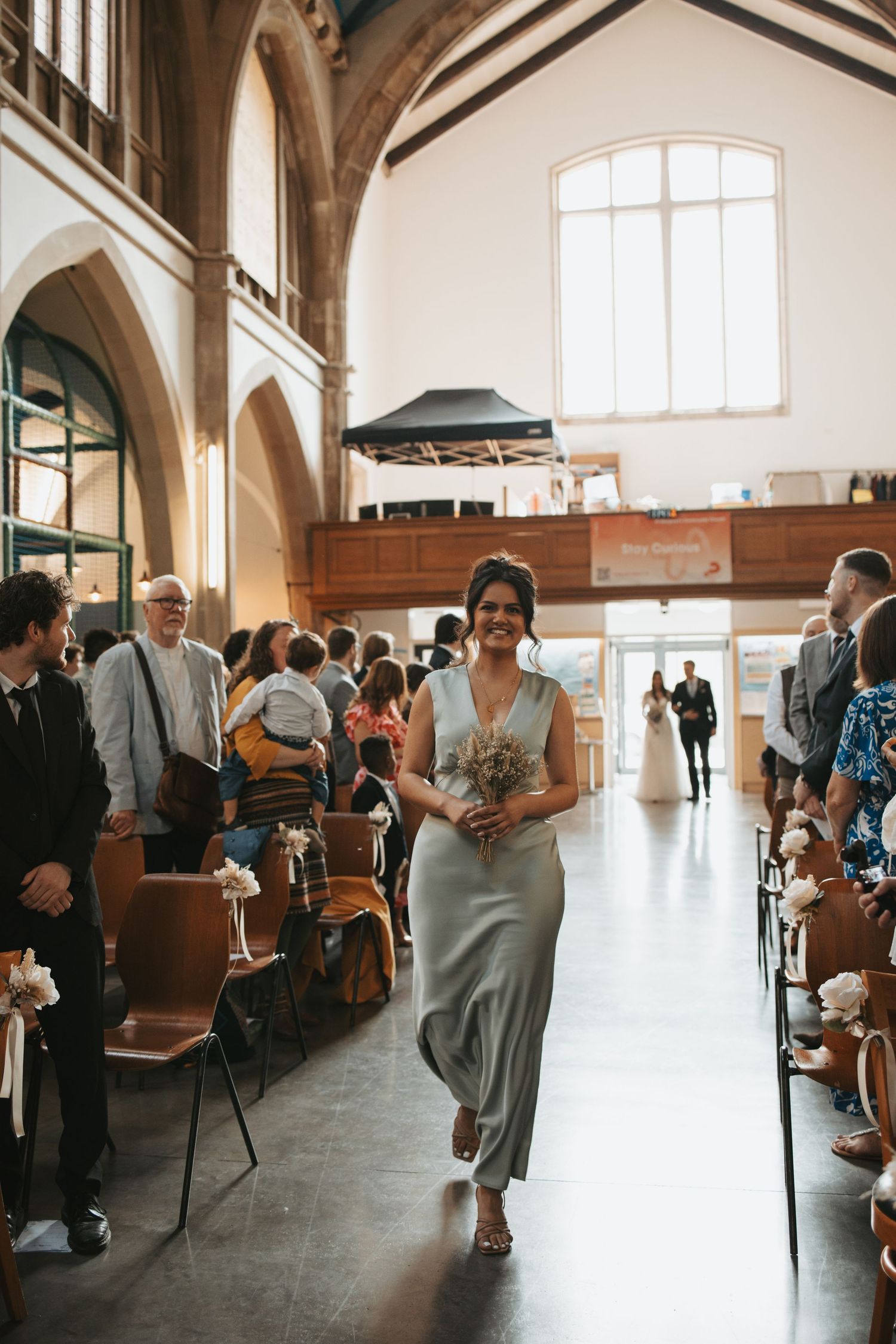 A wedding attendant walks down the aisle of a beautiful church with vaulted ceilings and arched windows.
