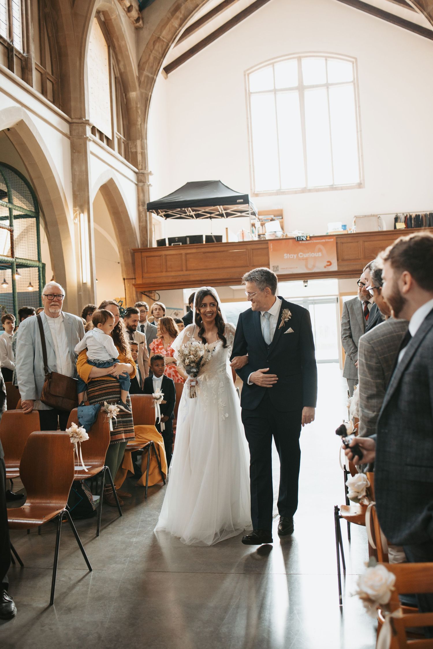 A wedding ceremony procession in a beautiful church with high ceilings and natural light streaming through windows.