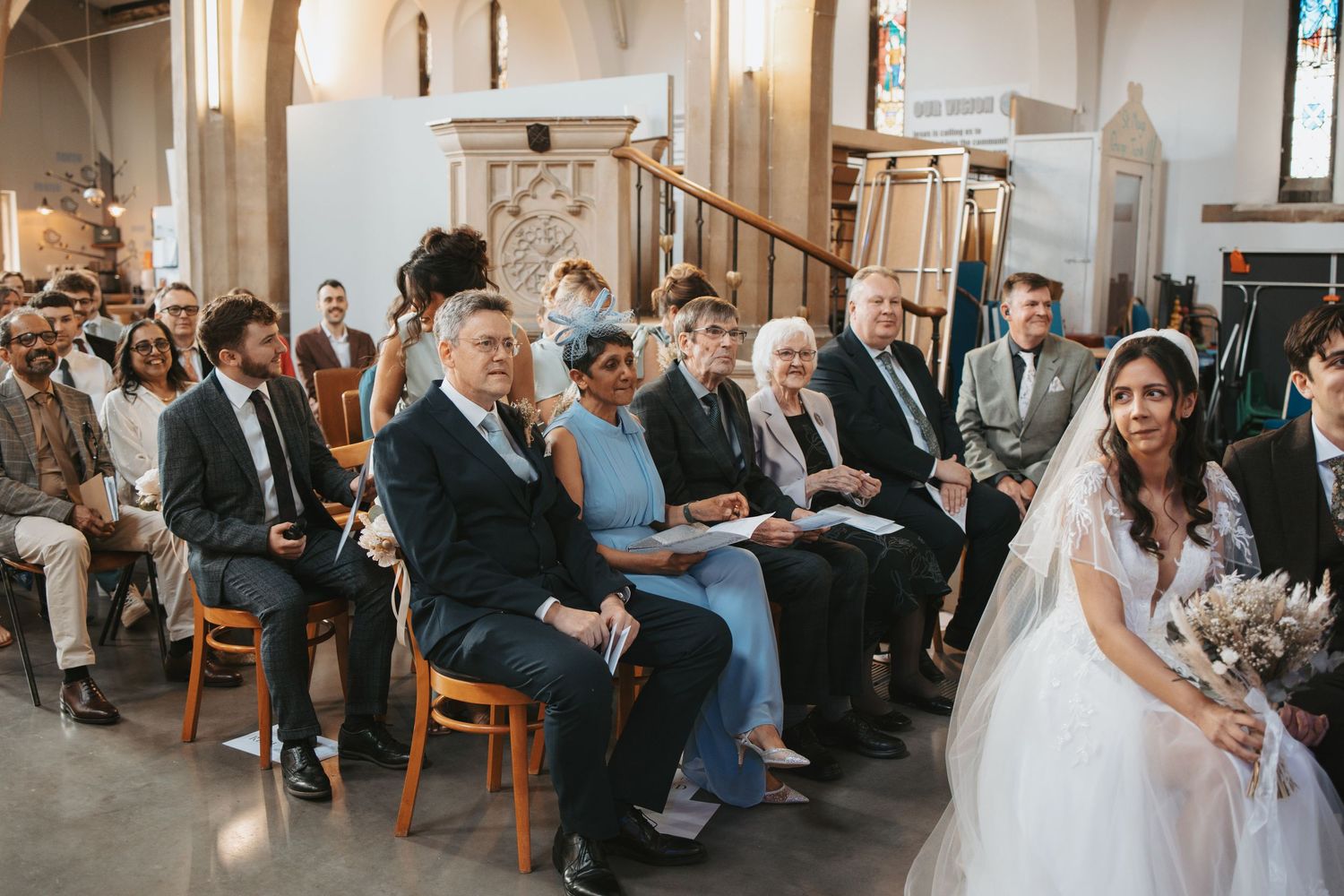 Wedding guests seated in wooden chairs inside a historic church with vaulted ceilings.