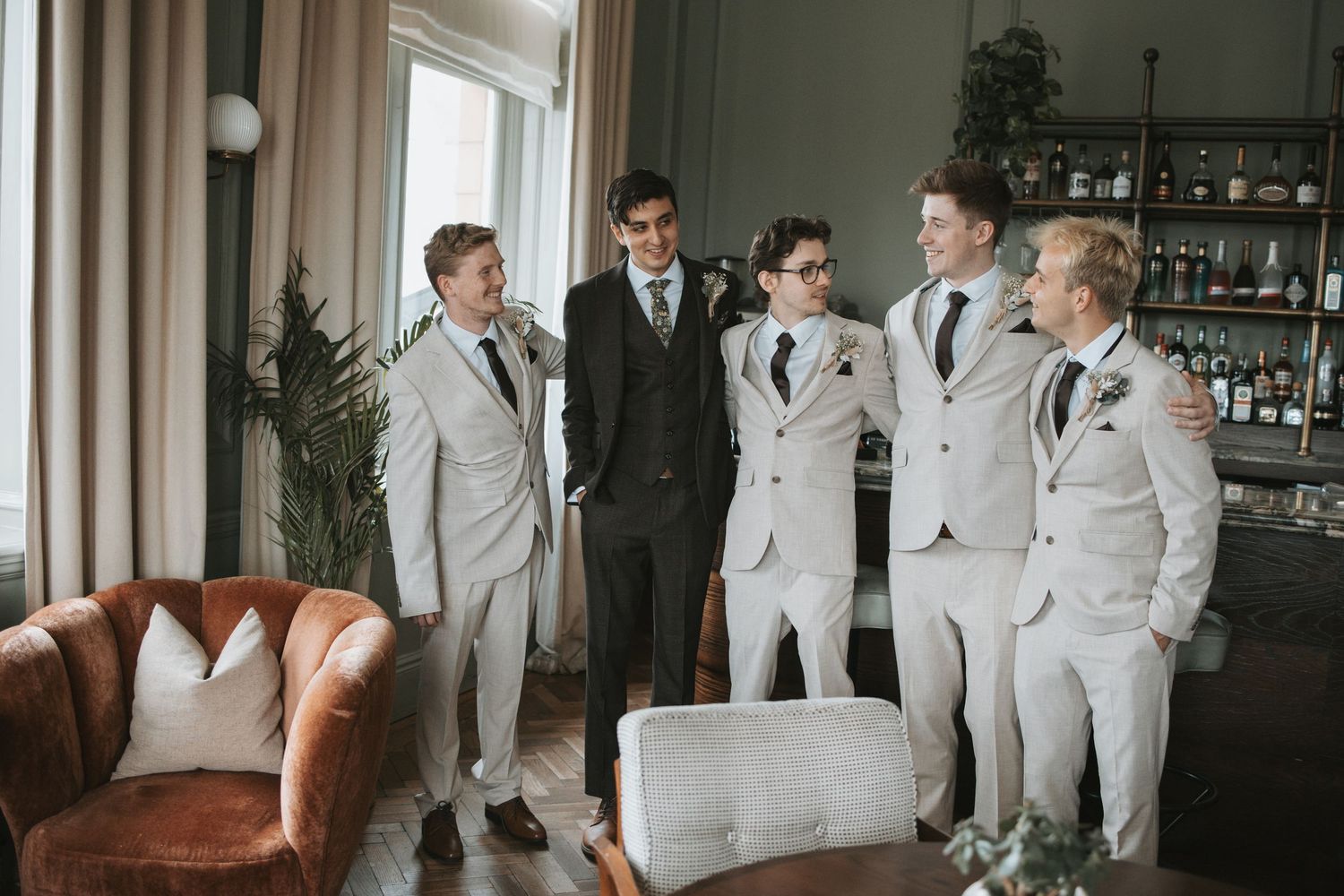 Wedding party in light gray suits gathered in a stylish room with vintage furniture.