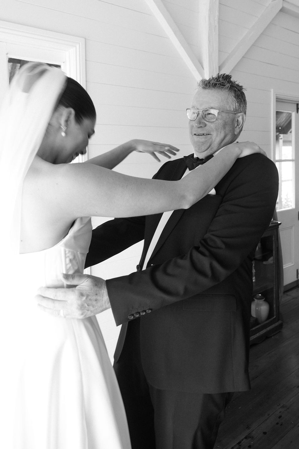 A heartwarming moment captured in black and white as a bride in white dress dances with an older gentleman in a suit.