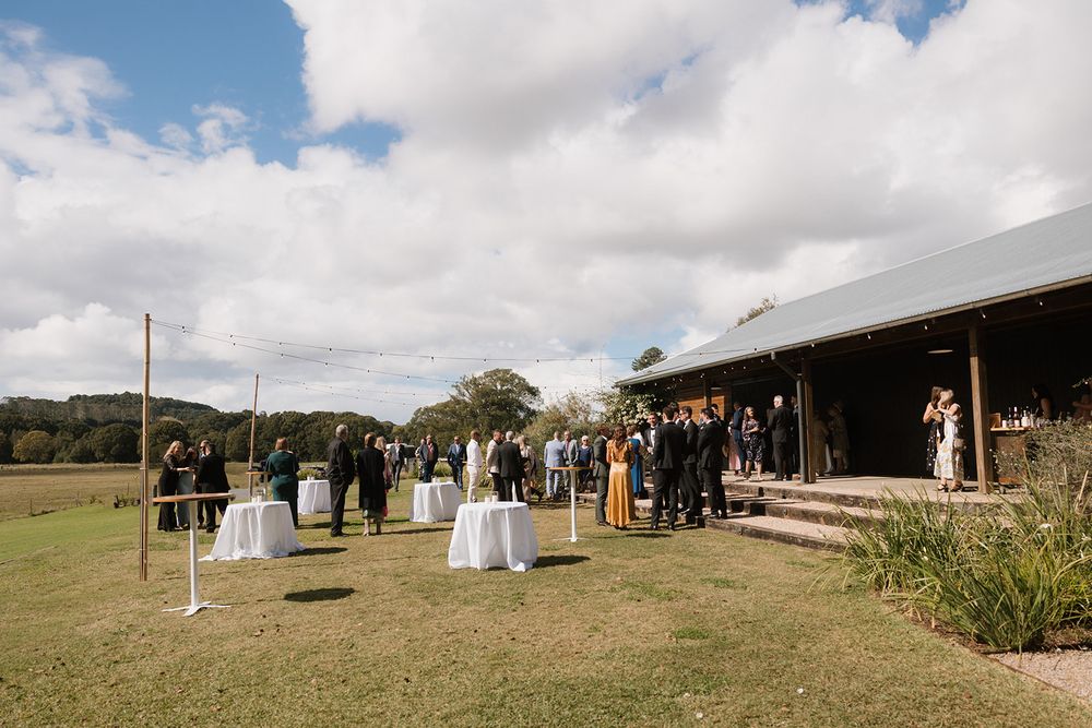 A panoramic view of an outdoor wedding venue with white tents and guests gathered on a grassy hillside.