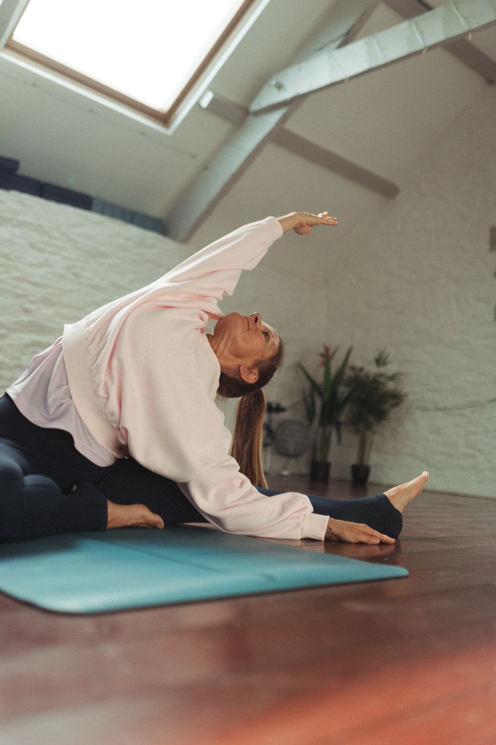 Person practicing yoga poses on a turquoise mat in a bright studio with white brick walls and wooden floors.