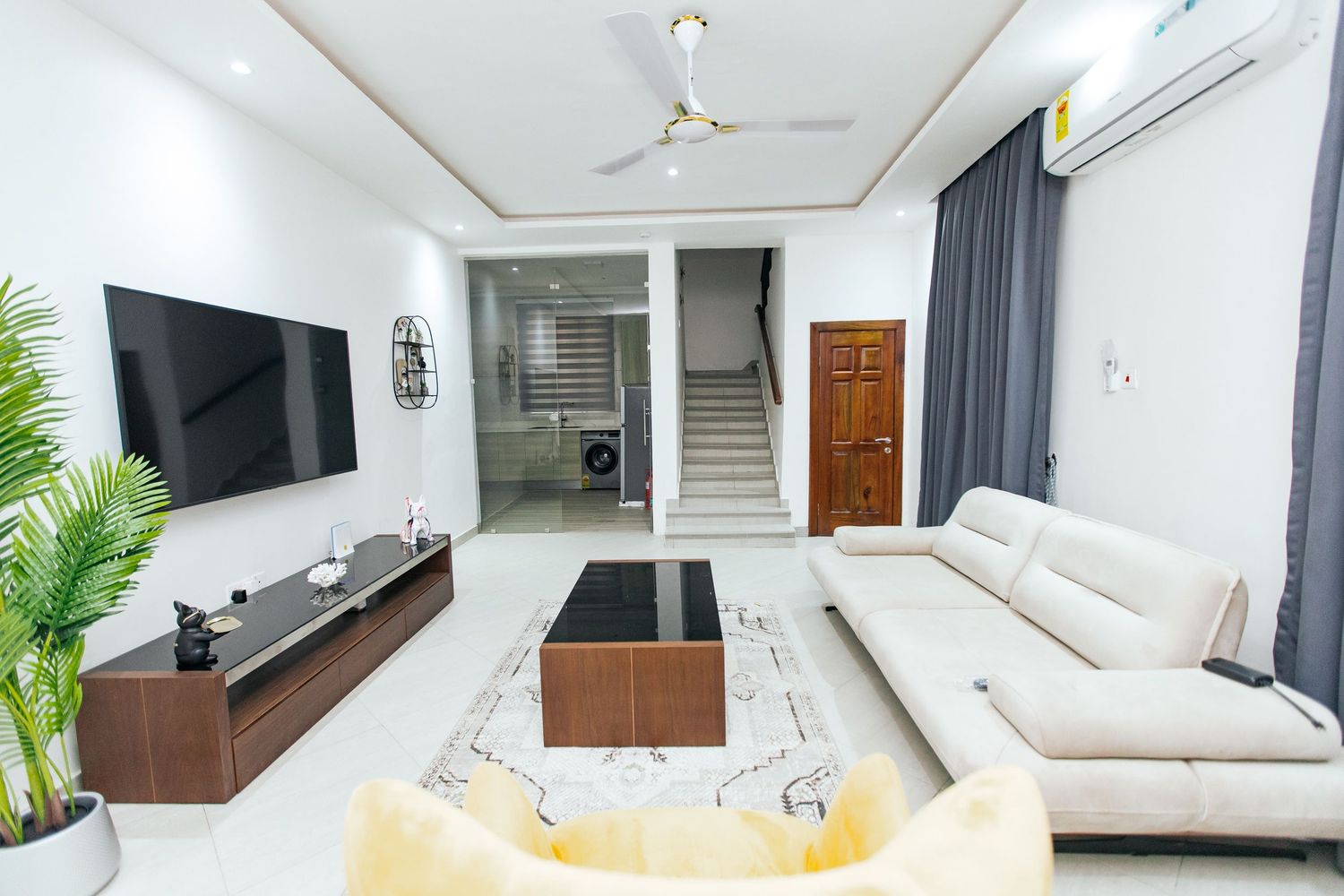 Bright living area with white walls, wooden furniture, and yellow accent chair creating a modern aesthetic.