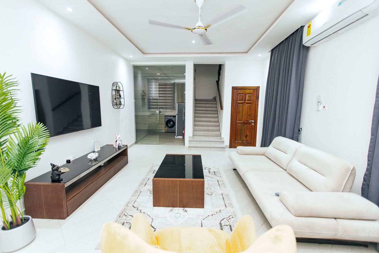 Clean white living room interior with ceiling fan, air conditioning, and modern entertainment setup.