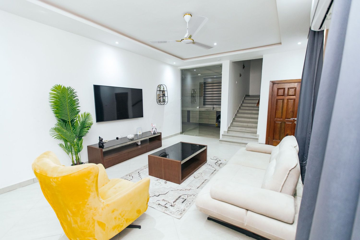 Spacious white room with modern entertainment center, grey drapes, and yellow accent furniture.