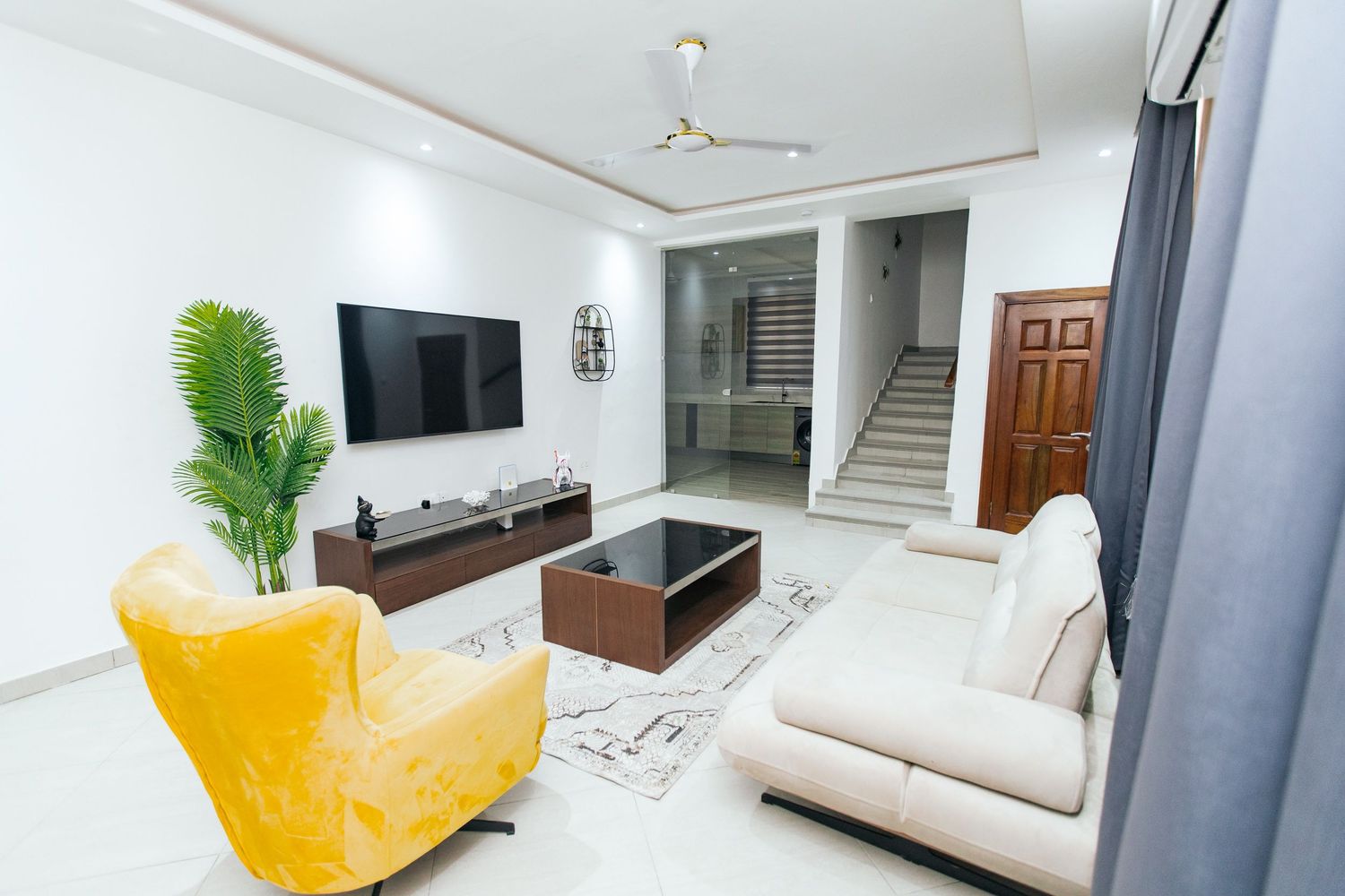 Contemporary living area with wooden TV console, white sofa, and tropical plant decoration.