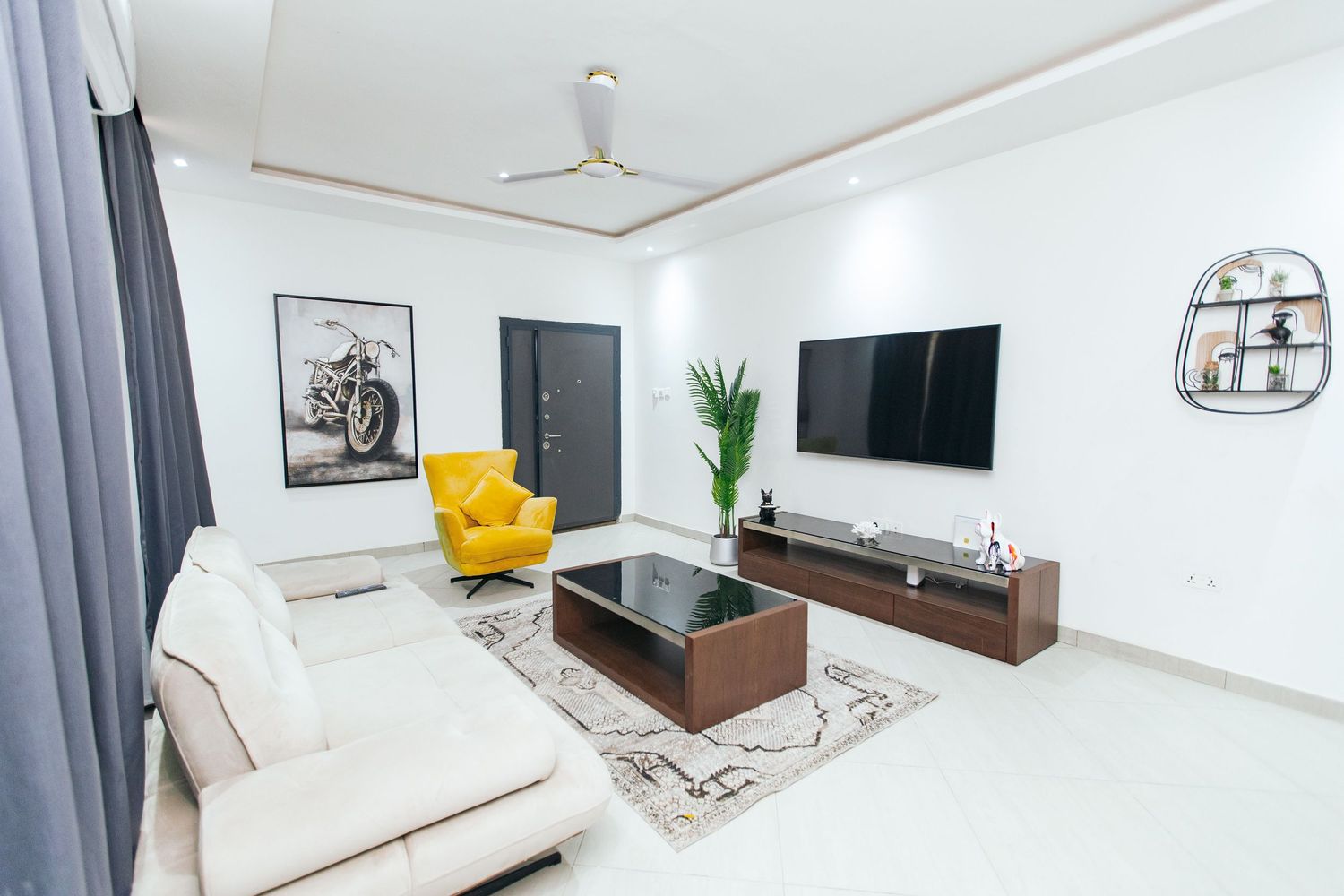 Modern white interior with mounted TV, wooden storage unit, and comfortable seating arrangement.